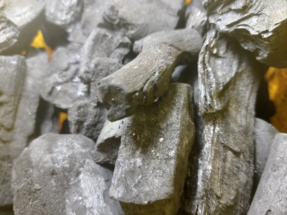 Grey-black lump charcoal stacked up with a yellow glow behind