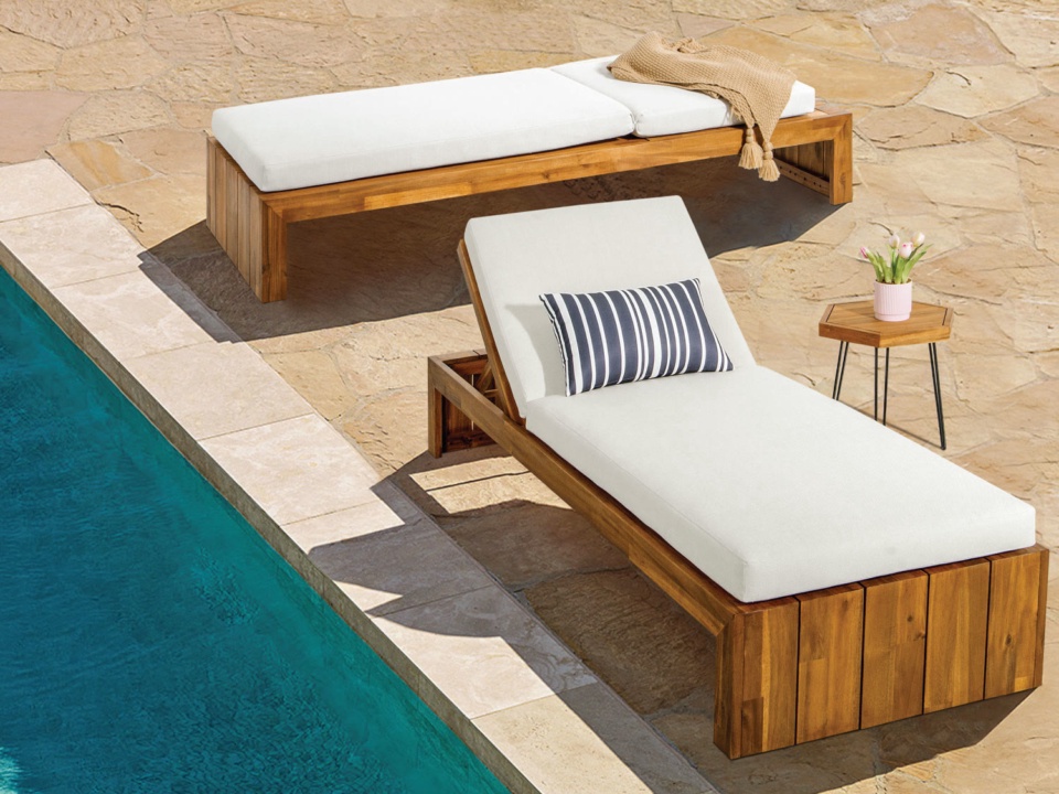 Two wooden sun loungers with white cushions and striped pillow beside a swimming pool