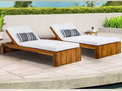 Two low wooden sun loungers with white cushions beside a pool