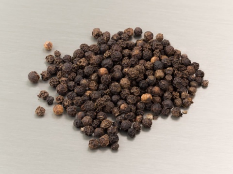 Pile of dried black peppercorns on a grey surface