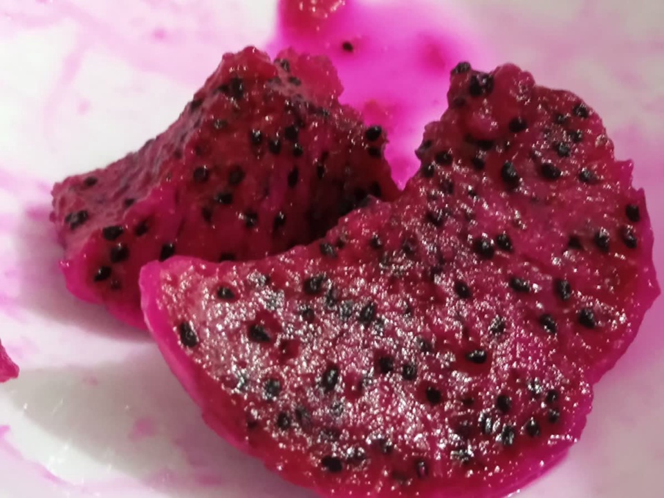Pieces of deep red dragon fruit flesh with black seeds on a white plate