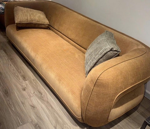 Long ochre sofa with a curved back on a wooden floor, full view
