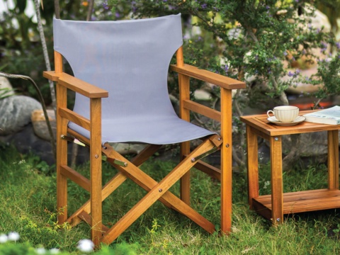 Director chair with wooden frame and grey fabric on grass beside a small table