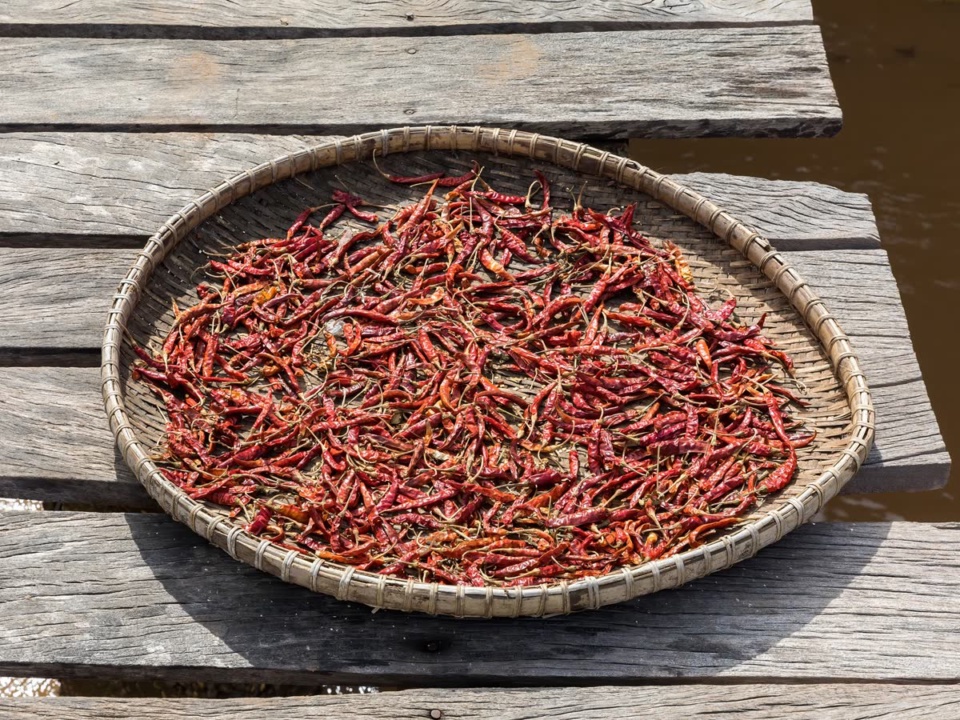 Small long dried red chillies in a bamboo tray on a wooden deck