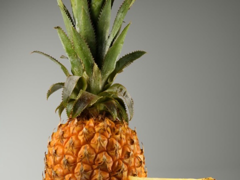 A whole pineapple with its green crown and a cut wedge beside it