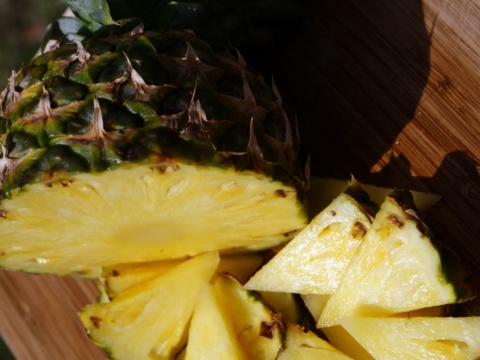 A halved pineapple showing yellow flesh on a wooden board