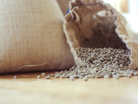 An open burlap sack with green coffee beans spilling onto a wooden table