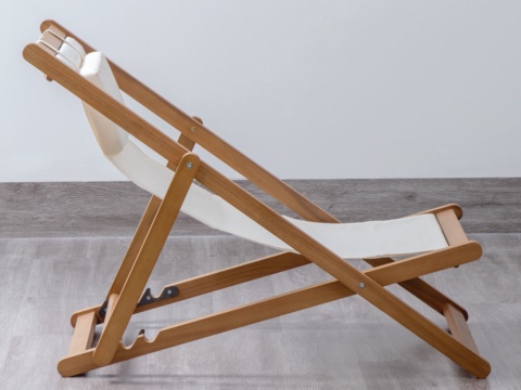 Side view of a cream canvas lounge chair with wooden frame, grey backdrop
