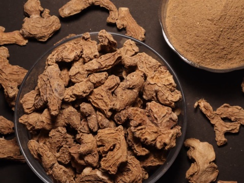 Dried ginger pieces in a glass dish beside a bowl of ginger powder