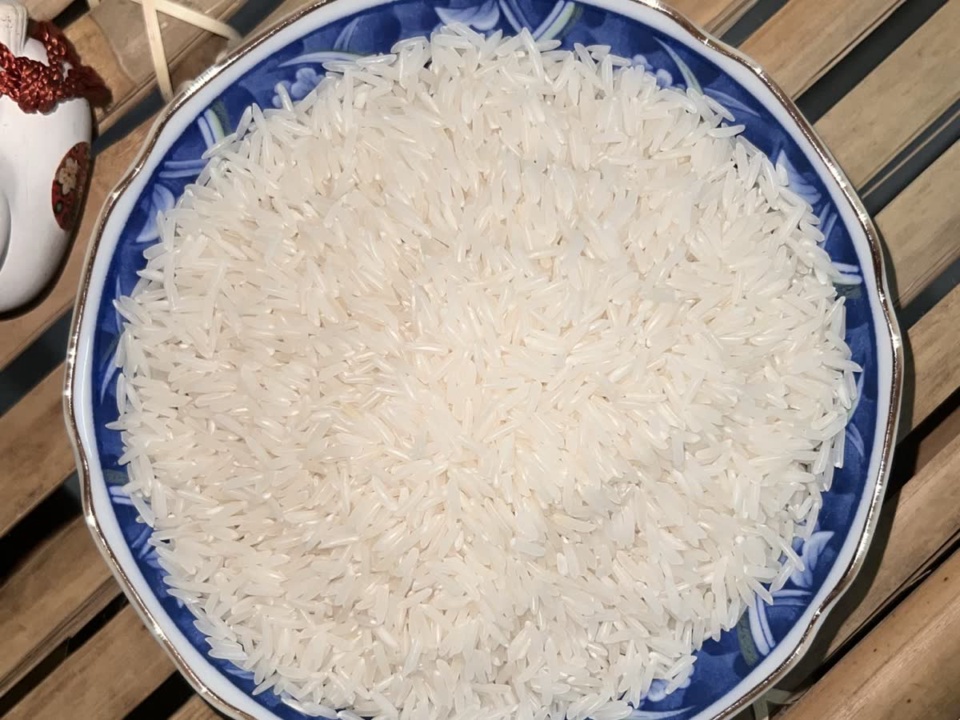 Long white rice grains in a blue patterned dish on a bamboo mat