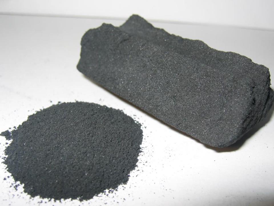 A porous grey-black carbon block with loose carbon powder beside it