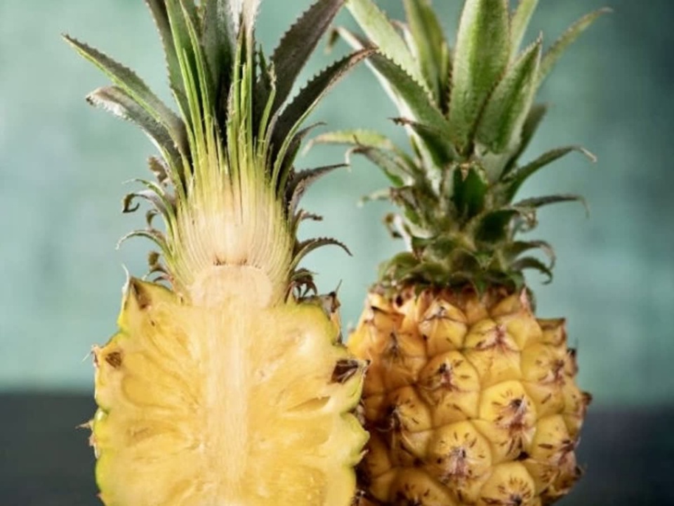 A halved pineapple showing yellow flesh beside a whole pineapple