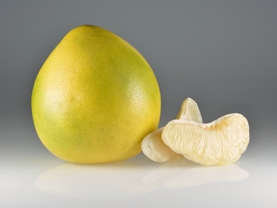 Yellow-green pomelo beside peeled segments on a grey backdrop