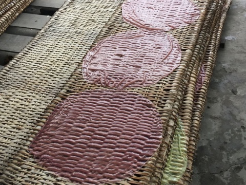 Round pink rice paper sheets drying on woven bamboo mats