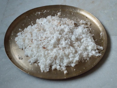 White grated coconut on a brass tray on a stone surface