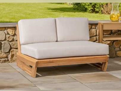 Two-seat wooden lounge chair with cream cushions by a stone wall