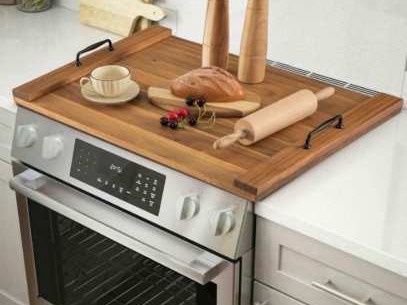 Wooden stove cover board with black handles holding bread and a rolling pin