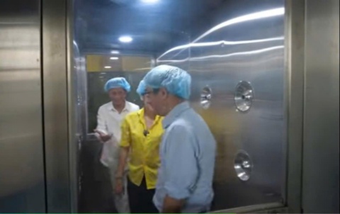 Ba người đội mũ trùm tóc đi qua buồng thổi khí bằng inox