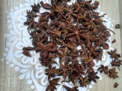 A heap of brown dried star anise spread on a light wooden surface