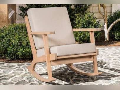 Light wooden rocking chair with beige cushions on stone paving